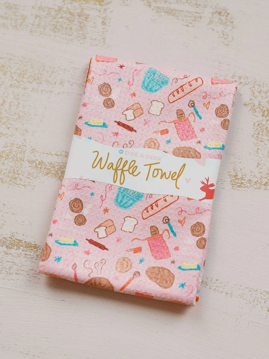 Waffle towel with bread-themed pattern on a light wooden surface