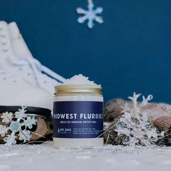 Candle jar with navy blue label 'Midwest Flurries' with decorative snowflakes and winter-themed elements in the background.