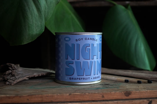 Candle in tin vessel. Blue label with blue text: night swim 