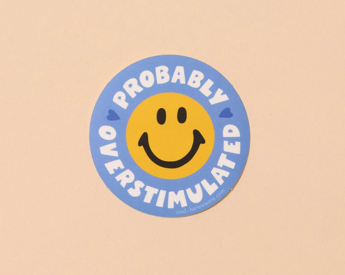 Circular sticker with smiley face and text 'Probably Overstimulated' on a beige background