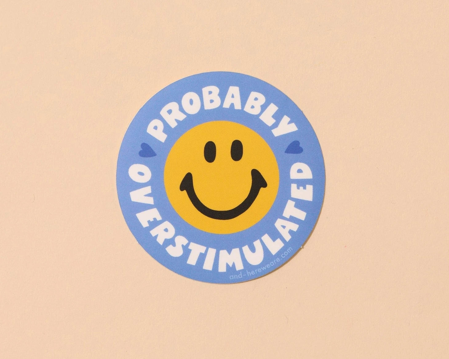 Circular sticker with smiley face and text 'Probably Overstimulated' on a beige background