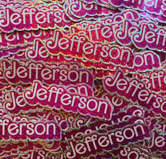 Pile of sparkly pink, silver, and white stickers. Stickers are die-cut and are in the shape of the word "Jefferson." 