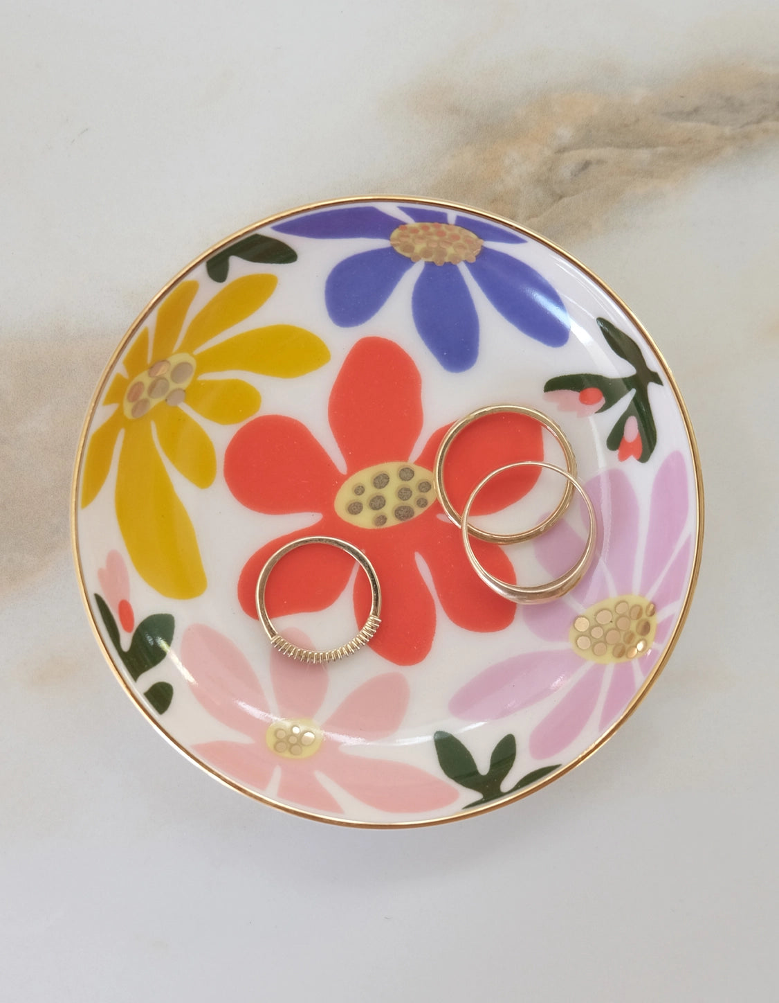 Floral-patterned trinket dish with gold rings on it 