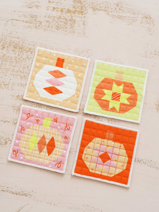 Four quilted coasters with pumpkin patterns on a wooden surface