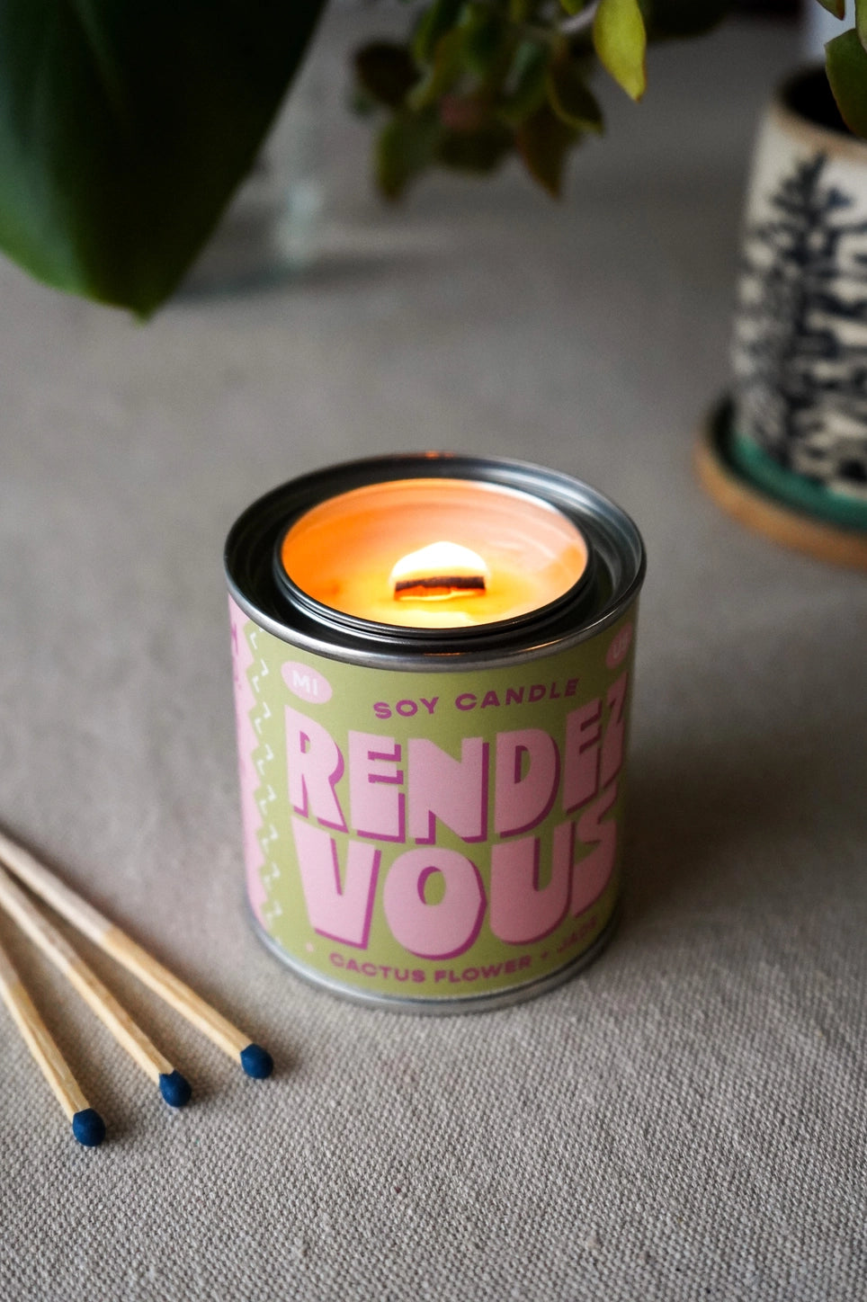 Candle in tin vessel. Green label. Pink text: rendezvous 