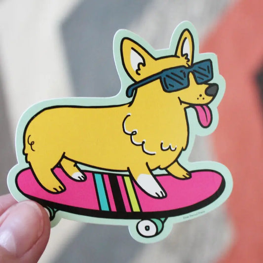 Corgi dog shaped sticker. Yellow dog with a pink tongue sticking out is wearing blue sunglasses. Dog is on pink skateboard. 