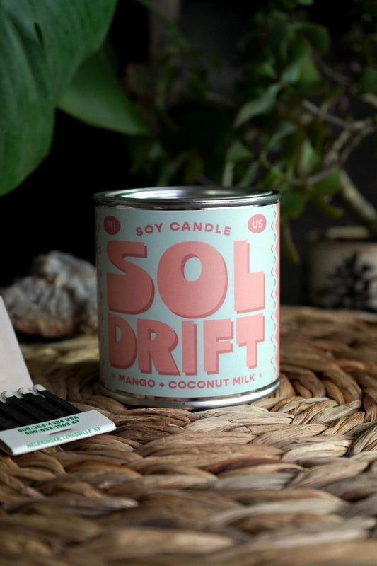 Candle in a tin vessel. Mint green label. Coral text: sol drift 
