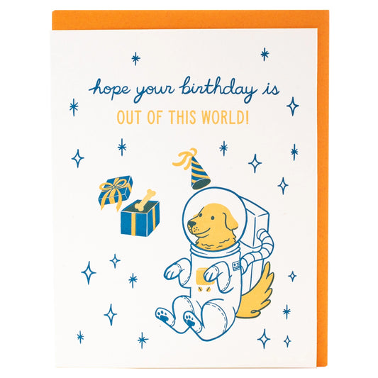 White greeting card with an illustration of a dog in a space suit. Blue and yellow text: hope your birthday is out of this world 