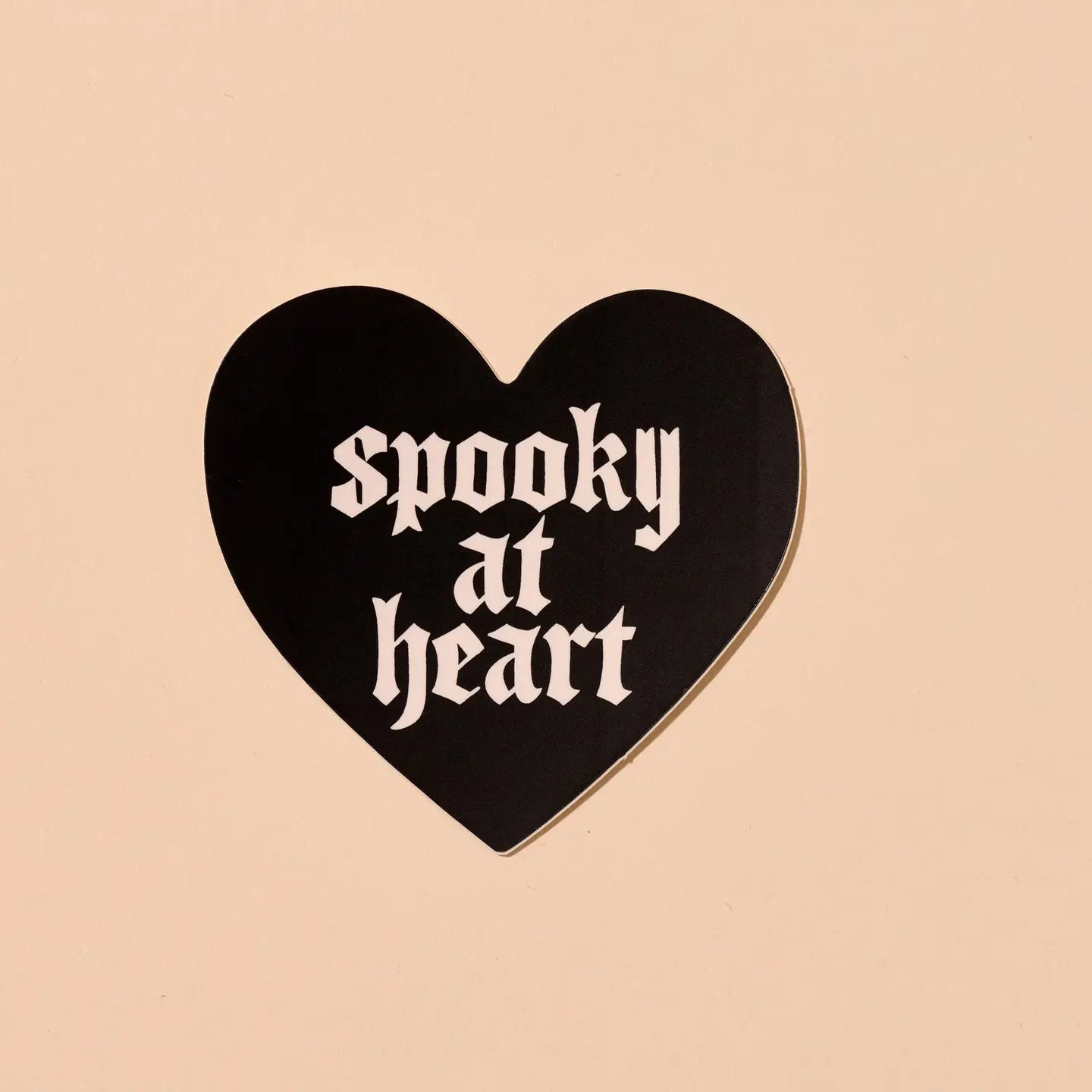 Black heart-shaped sticker with 'spooky at heart' text on a beige background