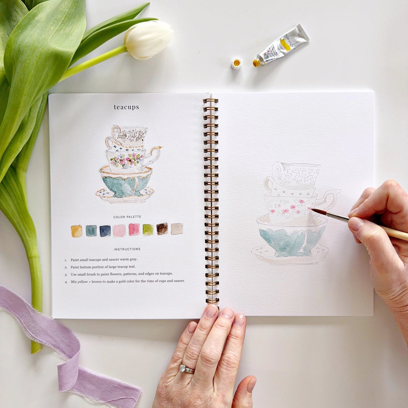 Person drawing teacups in a watercolor workbook 