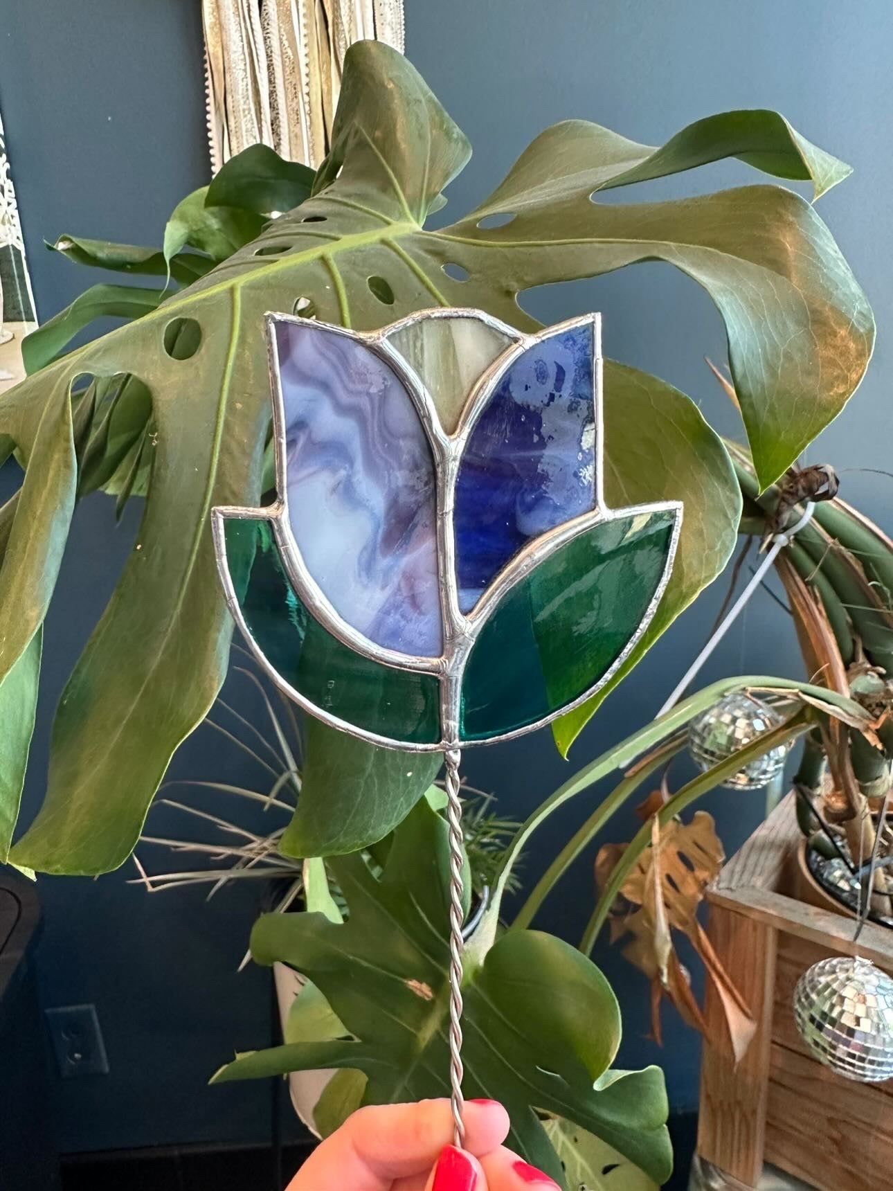 Stained glass lotus flower held in front of a green plant