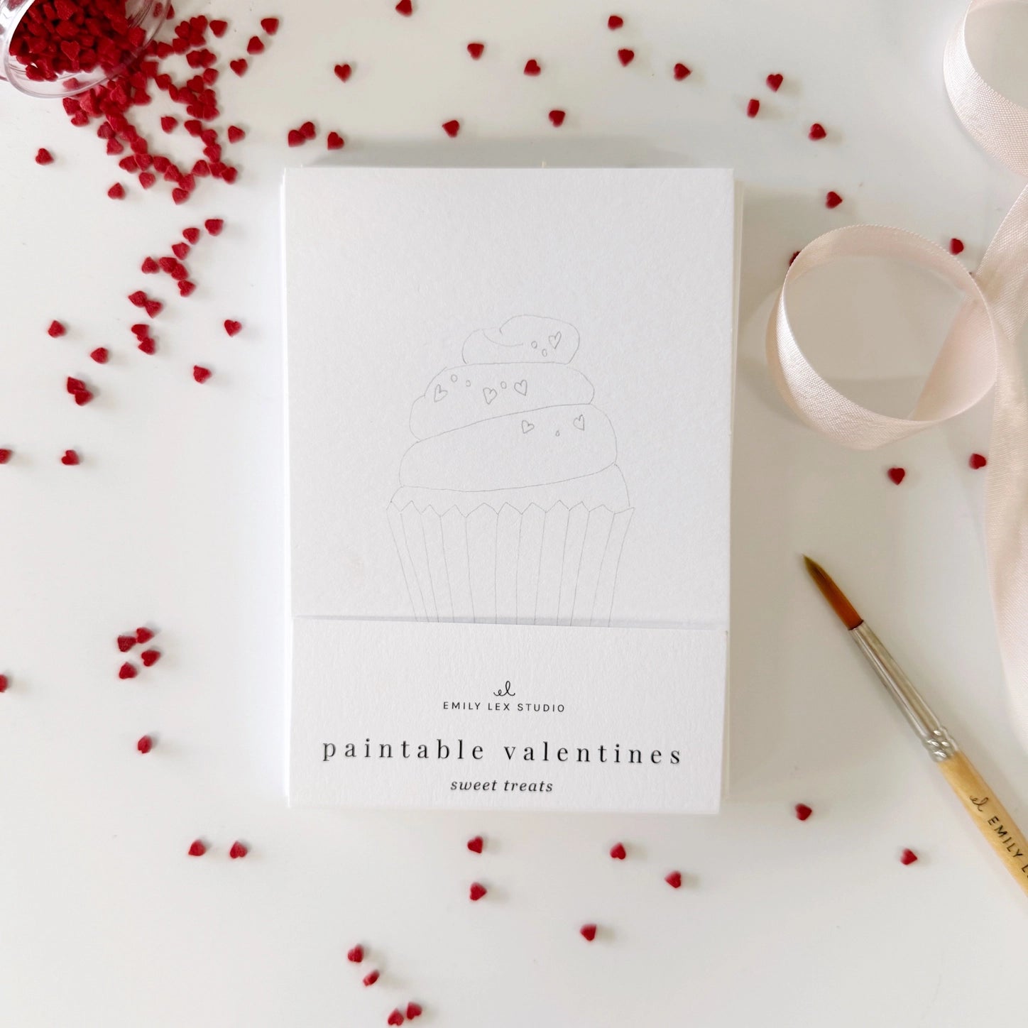 White notecard set with 'paintable valentines' text on a white surface with red heart decorations.