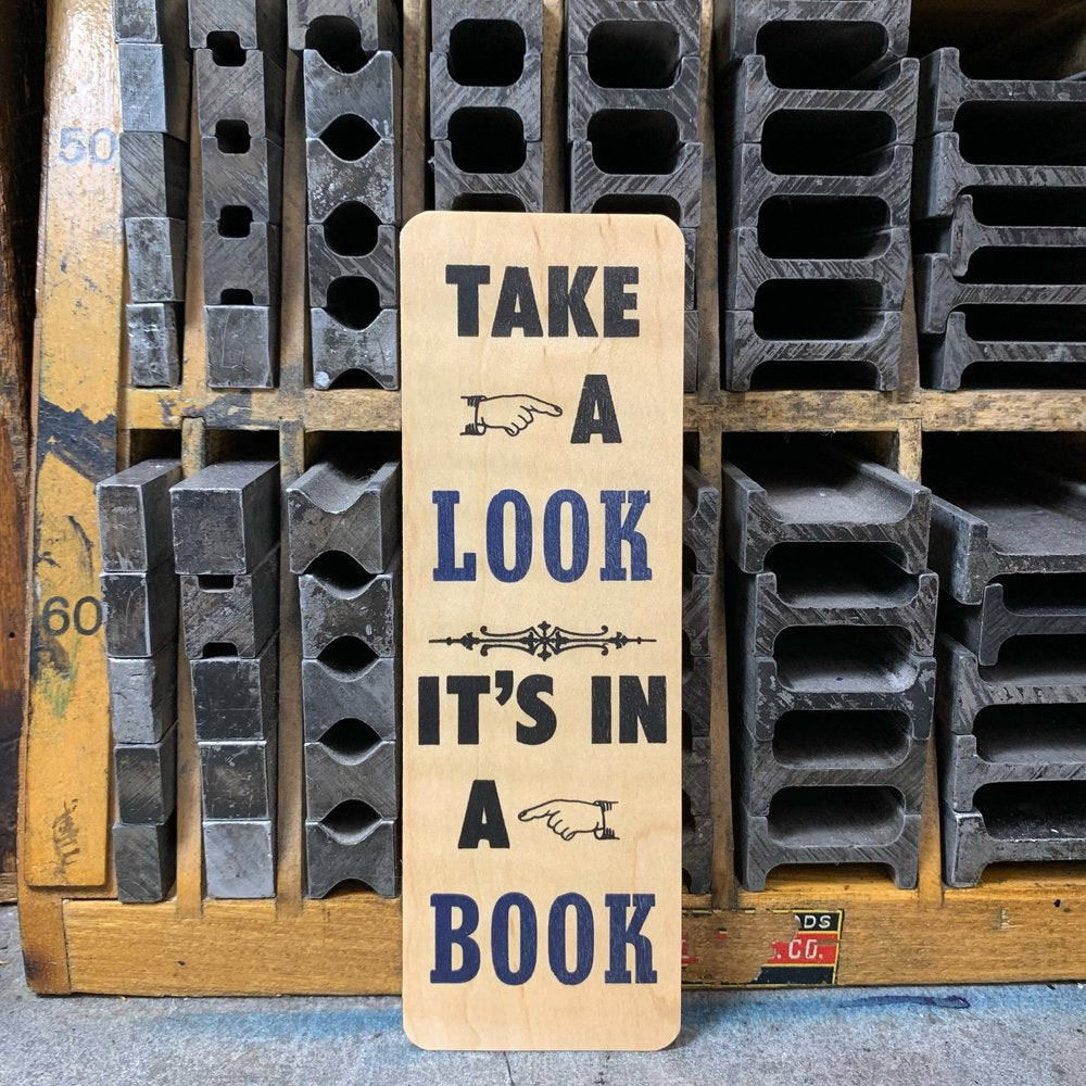 Wooden bookmark. "Take a look it's in a book" are letterpress printed in black and blue ink. 