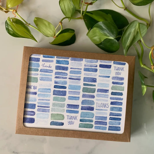 Card with blue pattern and 'THANK YOU' text, framed in brown box, with green leaves in the background.
