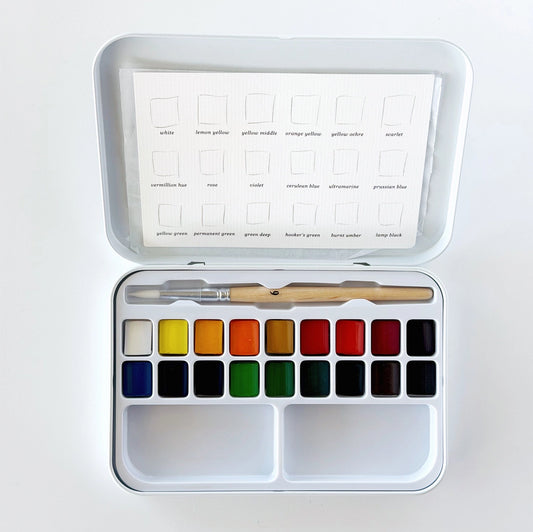 Watercolor paint set with color swatches and a brush in an white tin 