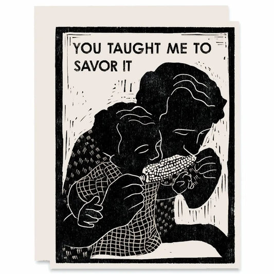 White card with black woodblock print of adult and child sharing a piece of corn on the cob. Black text "you taught me to savor it." 