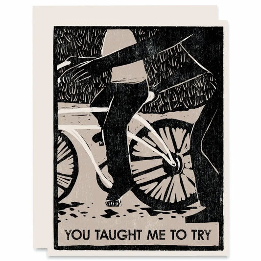 White card with black woodblock print of an adult helping a child ride a bike. Black text "you taught me to try" 