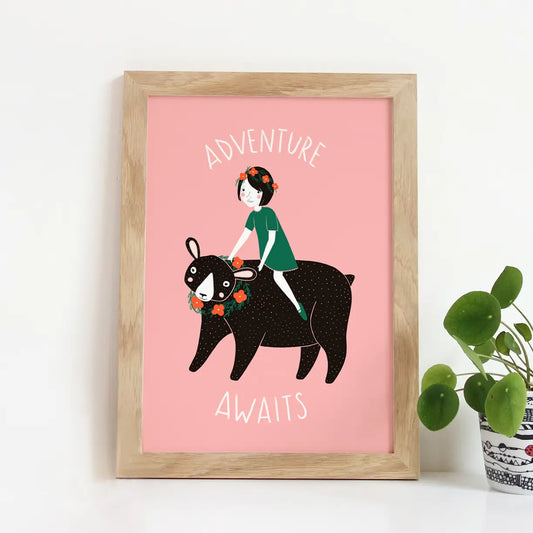 Art print with pink background and illustration of a kid on a black bear. White text reads "adventure awaits" 