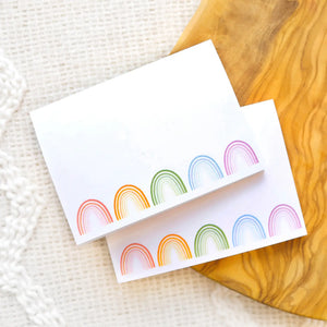 Pads of white sticky note paper with red, orange, green, blue, and purple rainbows on the bottom edge