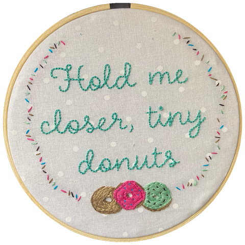 Embroidery hoop with white fabric and teal thread reading Hold Me Closer Tiny Donuts