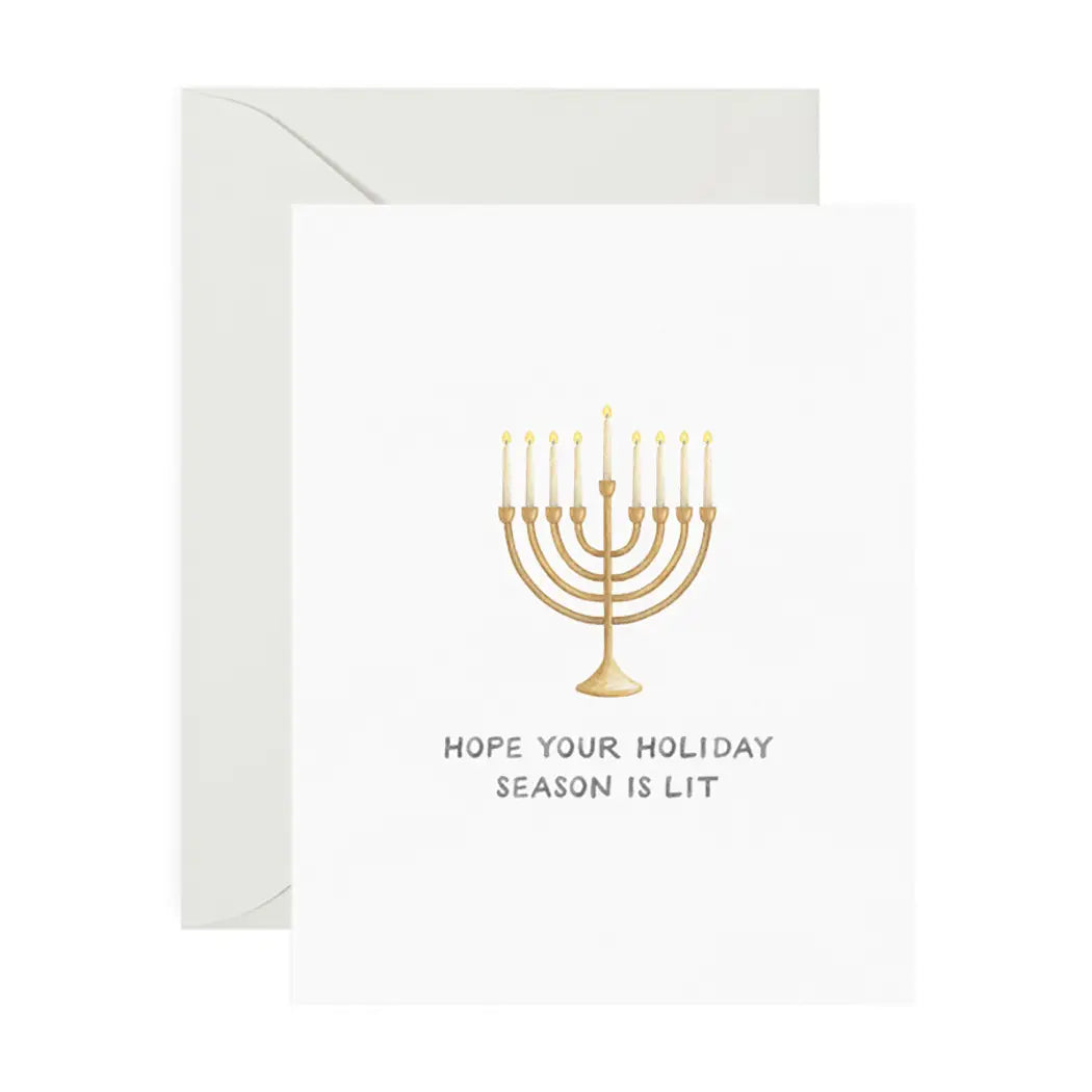 White card with drawing of gold menorah and white candles. Black text reads "hope your holiday season is lit" 