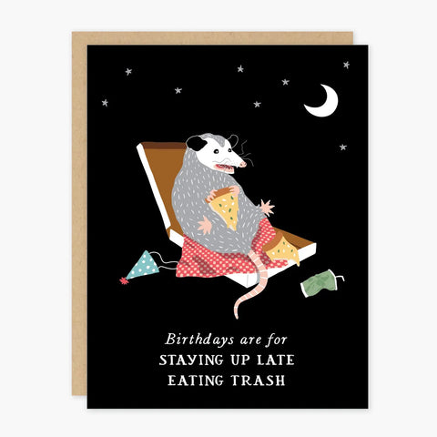 Black card featuring a possum eating pizza out of a box. White text reads "birthdays are for staying up late and eating trash." Card is white inside.