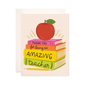 White card with a stack of books and an apple. Black text on the book spines reads "thank you for being an amazing teacher"