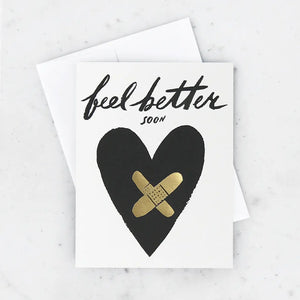 White card with illustration of a black heart with gold foil bandaids. Black text reads "feel better soon" 