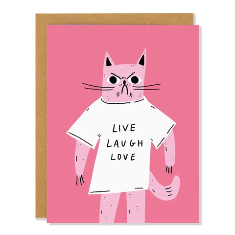 Pink card. Drawing of an angry light pink cat wearing a white t-shirt. Black text on the tshirt reads "live laugh love." Inside of card is white.