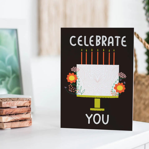 Black card with white birthday cake decorate with candles and flowers. White text reads "celebrate you"