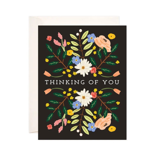 White card with a black background and white, blue, yellow, and pink florals. White text reads "thinking of you." 