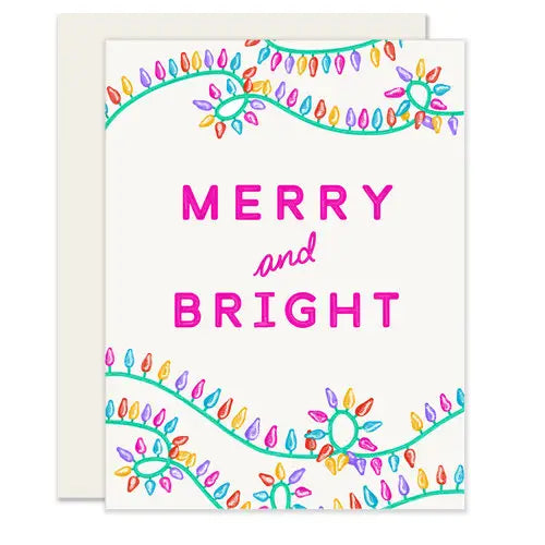 White card with pink text reading "merry and bright." Pink, purple, turquoise, and yellow holiday lights