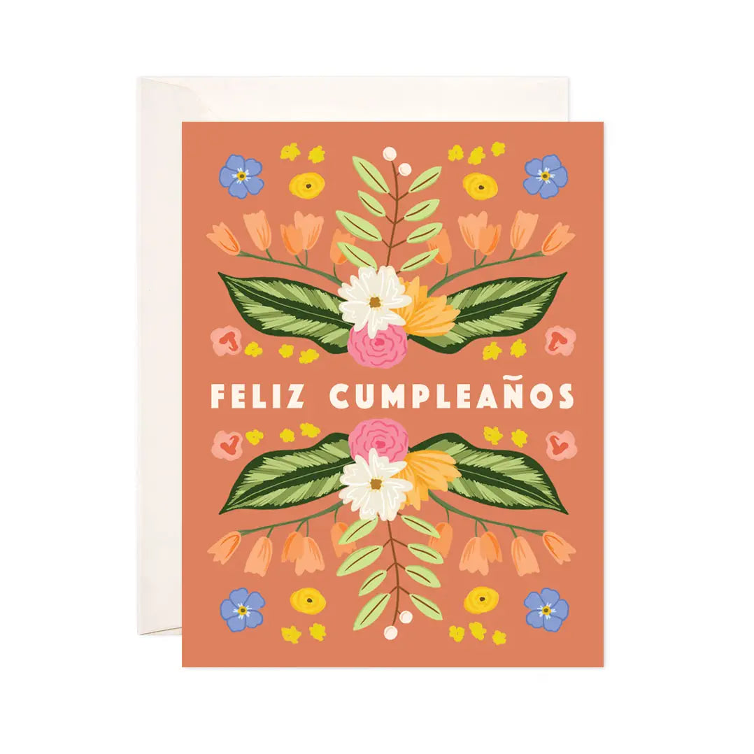 White card with an orange background and illustration of white, pink, orange, blue, and green florals. White text reads "feliz cumpleanos"