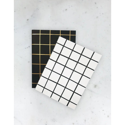 Two small notebooks. One is black with gold gridlines and the other is white with black gridlines 